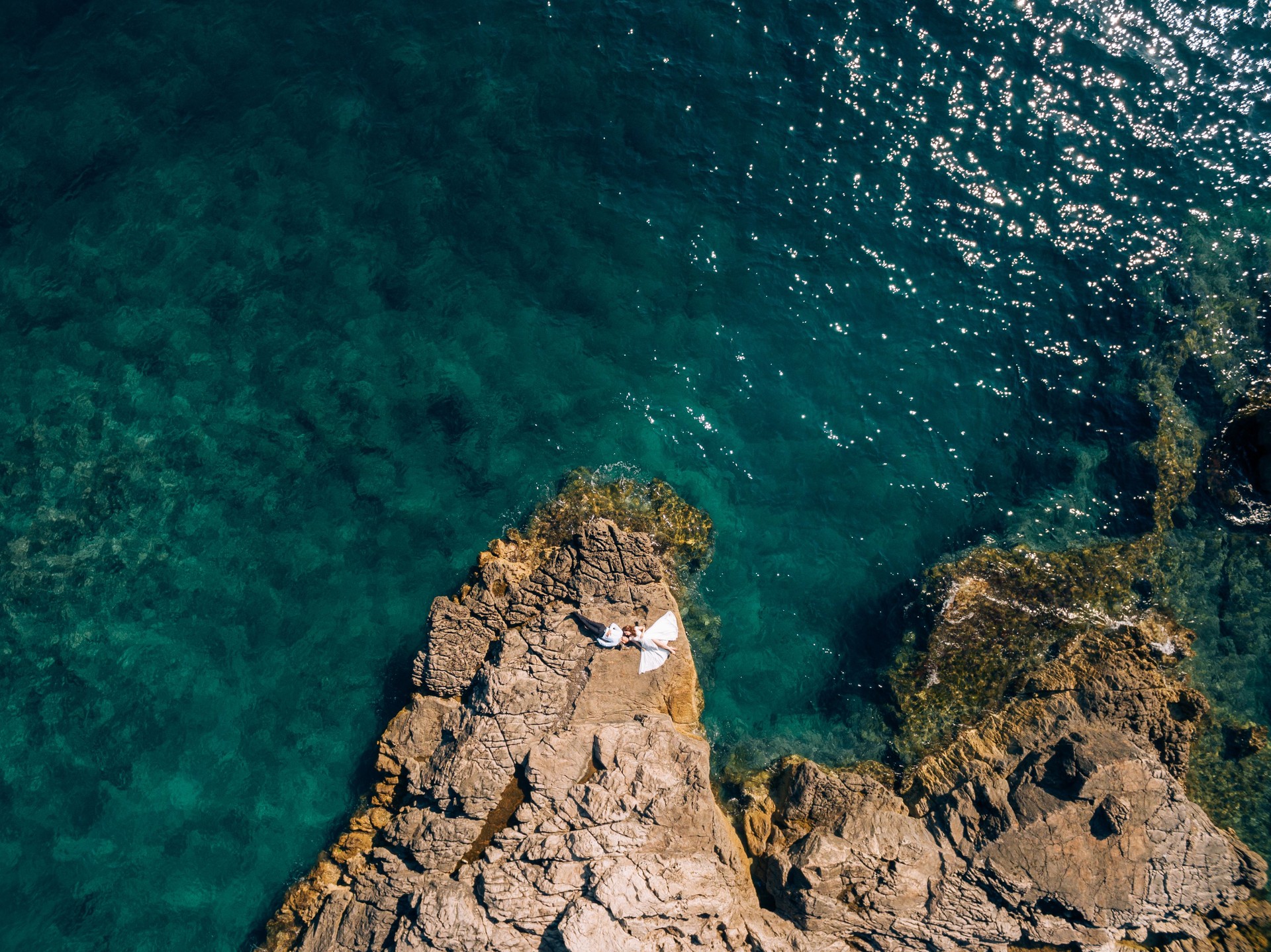 Bride and groom lie on a rocky cliff. Aerial view