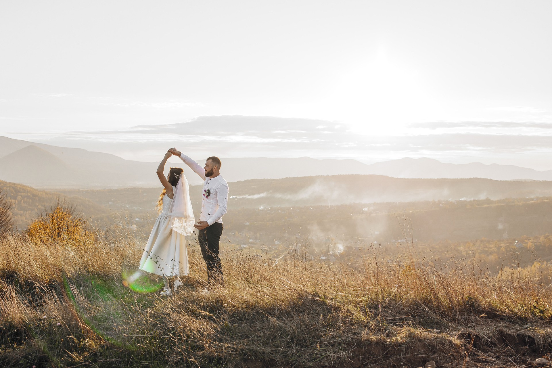 A bride and groom are dancing in a field with mountains in the background
